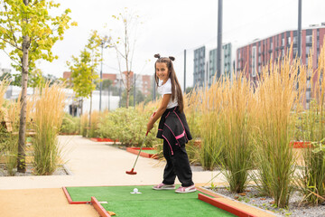 Cute preschool girl playing mini golf with family. Happy toddler child having fun with outdoor...