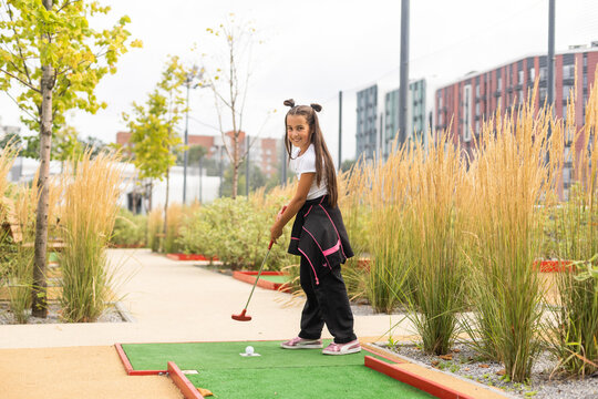 Cute preschool girl playing mini golf with family. Happy toddler child having fun with outdoor activity. Summer sport for children and adults, outdoors. Family vacations or resort