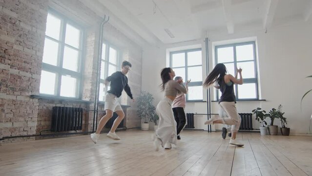 Low wide angle slow motion of young cheerful people dancing vogue in studio in daylight