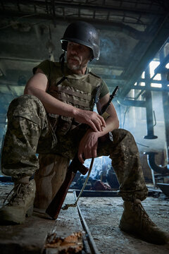 A Ukrainian Soldier In A Helmet And Bulletproof Vest Smokes A Cigarette In A House Destroyed By A Bomb.