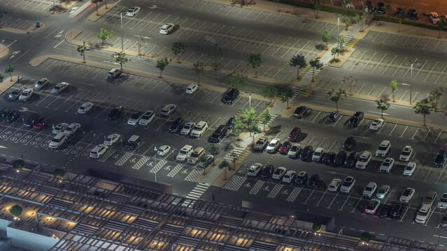 Big parking lot near mall crowded by many cars night timelapse aerial view. Vehicles moves in and out