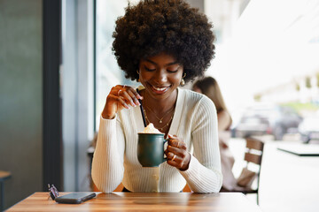 Young afro woman taking break and drinking coffee in cafe