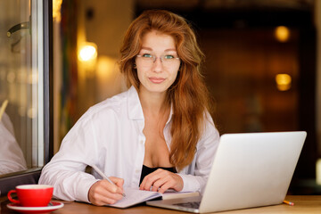 Young beautiful smiling businesswoman working with laptop looking into camera