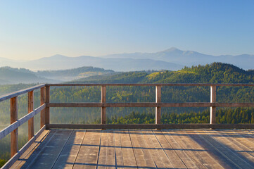 Early morning view from the wooden terrace on Carpathian mountain range. Sunbeams falling on the balcony, blue mountain peaks in the background.