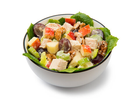 Chicken Waldorf salad of apples, celery stalks, walnuts, grapes, lettuce in a white salad bowl isolated on white background.