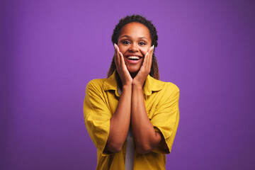 Overjoyed young casual African American woman with smile puts palms to cheeks feels pleasant...