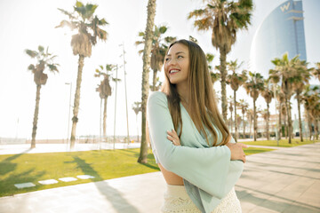 Fototapeta na wymiar Cheerful caucasian girl laughing looking away spending leisure time outdoors in summer day. Long-haired girl keeps hands in her waist, wears shirt. Sincere emotions concept