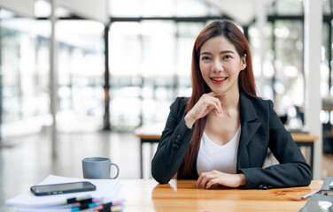 Confident smiling businesswoman looking at camera , sitting at her workplace at modern office.Blurred background