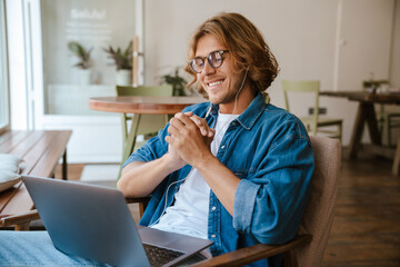 Young long-haired man in headphones with folded hands watching laptop