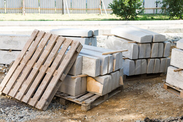Reinforced concrete blocks neatly stacked on the territory of a fenced construction site, a curb stone on wooden pallets for road repairs.