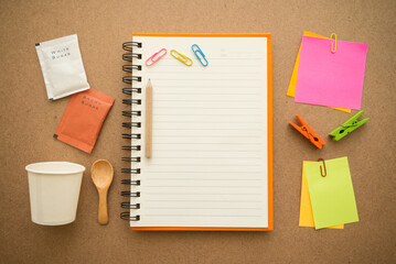 Flat lay of blank lined paper notebook with coffee cup, sugar and office supply, stationery, accessories on cork board background. Lifestyle, creative idea, business and education concept.