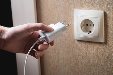 A young woman inserts a plug into a socket. A young woman plugs a charger or electrical appliance power cord into a socket. High quality photo