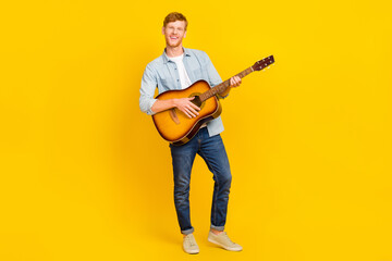 Photo of cute pretty guy dressed denim shirt playing guitar singing smiling isolated yellow color background