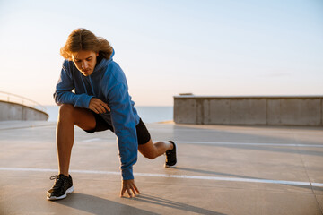 Young blonde man doing exercise while working out on parking