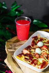 colombian street food, salchipapa served on a wooden tray with a glass of red fruit juice next to it. fast food with potato, sausage, egg and sauces.