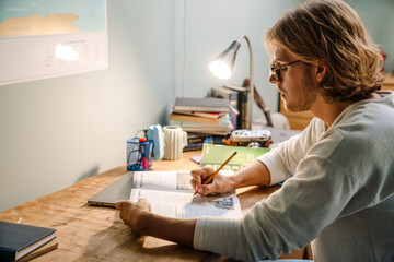 Blonde bristle man doing homework while sitting at table at home