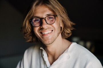 Blonde man in eyeglasses smiling and looking at camera at home
