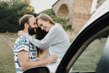 Caucasian man and woman hugging on the hood of car, middle-aged couple enjoying road trip together