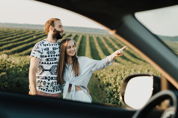 View through car window, happy middle-aged couple hugging together in the beautiful fields,...