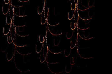 Luz de neón en movimiento y velocidad en bokeh, mostrando líneas punteadas arqueadas colgando como guirnaldas, formando un hermoso y original diseño abstracto con fondo negro