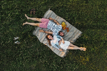 Aerial shot top-down view of middle-aged couple enjoying picnic in the field, caucasian man and woman lying on a blanket