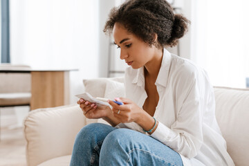 Young black woman being upset while holding pregnancy test at home