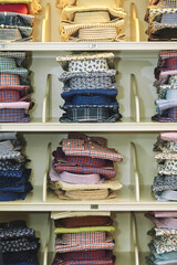 Showcase with many various folded male fashion shirts for men in stock on shelves in menswear store clothing shop