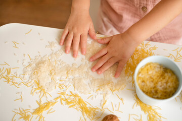 Obraz na płótnie Canvas Baby hands playing with grain, nuts, pasta and rice at table.Sensorial early development, education for baby, child.Kid useful games.Fine motor skills concept.Top view.