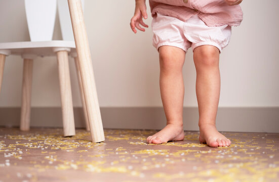 Toddler girl legs standing on messy floor after playing with grain, nuts, pasta and rice.Sensorial early development, education for baby, child.Kids dirty room concept.