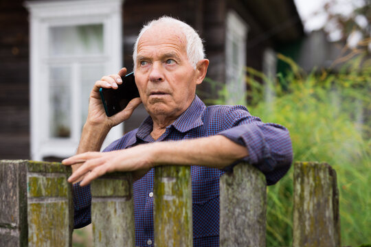 Elderly man standing beside his house and talking on phone