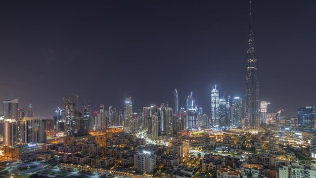 Dubai Downtown during all night with moon and lights turning off timelapse with tallest skyscraper and other illuminated towers panoramic view from the top in Dubai, United Arab Emirates.