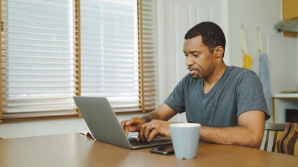Concentrated Black African American man using laptop computer at home, Work at home, Freelancer typing on keyboard, Lifestyle