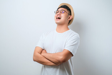 Portrait of young handsome Asian man wearing casual shirt and bucket hat standing with arms crossed and smiling at camera