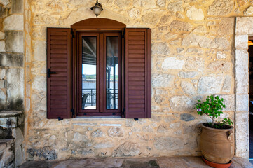 Fototapeta na wymiar Window detail of a stone cottage facade with plant pot besides. Greece, Crete. 