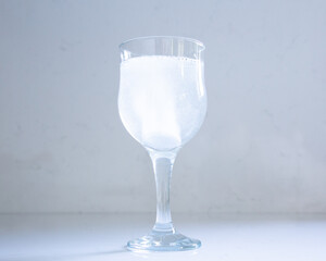 Selective focus closeup of stem glass set on quartz background, with effervescent antacid tablet dissolving in water