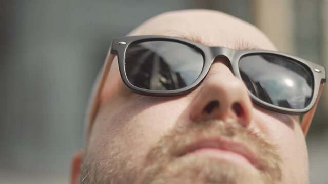 Close-up of a man wearing sunglasses in the reflection of a business center. A businessman looks around and looks for a solution to a problem in the cityscape. High quality 4k footage