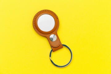 Closeup top view of a brown leather case with white Bluetooth tracker on the yellow background