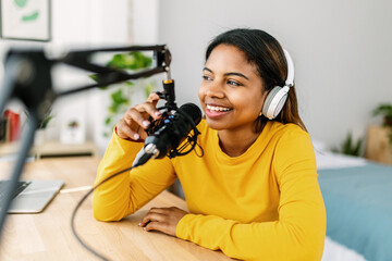 Young ethnic woman recording radio podcast - Millennial female content creator working from home...