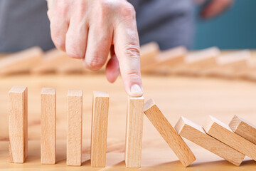Businessman stopping wooden block from falling in the line of domino with risk concept