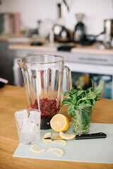 Making summer refreshing cocktail in process: raspberries in a blender, mint, knife, lemon and ice on the background on the table, vertical photo 
