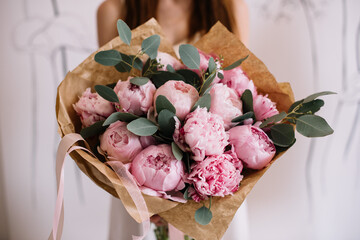 Very nice young woman holding big and beautiful mono bouquet of fresh pink peonies and eucalyptus,...