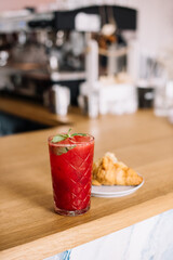 Delicious fresh red strawberry and basil lemonade with almond croissant on the wooden bar counter, vertical view