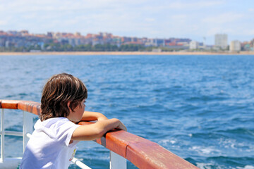 A little boy leaning out of the stern of a ship