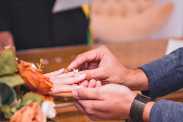 Obraz na płótnie Canvas two hands at the moment of exchanging rings between the bride and groom next to a bouquet of flowers