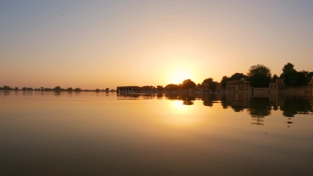 4K View of the Gadisar Lake during sunset with chhatri in the middle of the lake at Jaisalmer in Rajasthan, India. Reflection of the Chhatri pavilion in the orange water of the lake during sunset.	
