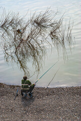 view from above the fisherman catches fish on a fishing rod and sits on a chair, fishing on the river bank in the morning. spring fishing in nature.