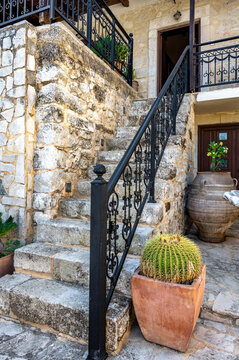 Stair detail with vlack metal rails of a stone cottage facade with plant cactus pots besides. Greece, Crete.