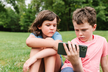 Siblings using smartphone together in park