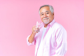 happy asian old man hand holding glass of water drinking smile wearing pink shirt and pink black background.