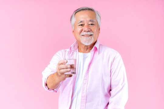 Happy Asian Old Man Hand Holding Glass Of Water Drinking Smile Wearing Pink Shirt And Pink Black Background.